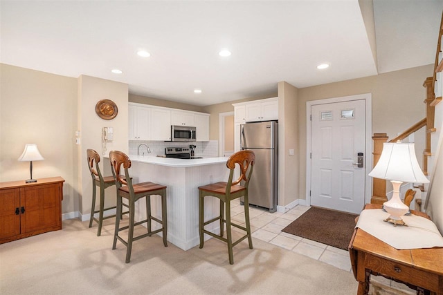 kitchen with appliances with stainless steel finishes, a breakfast bar, a peninsula, white cabinetry, and decorative backsplash