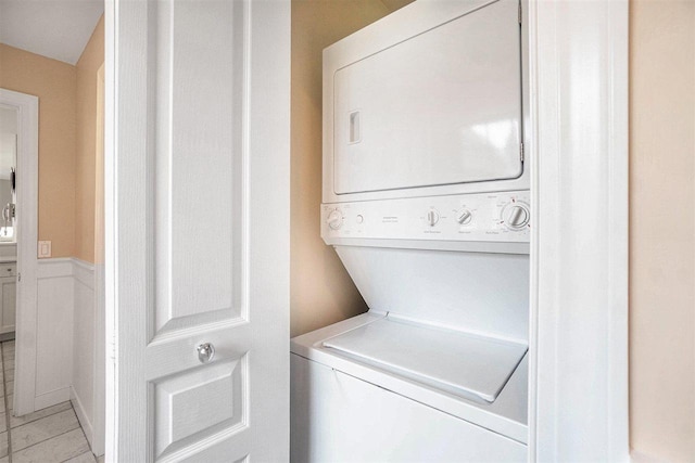 laundry room featuring laundry area, wainscoting, stacked washing maching and dryer, and light tile patterned floors
