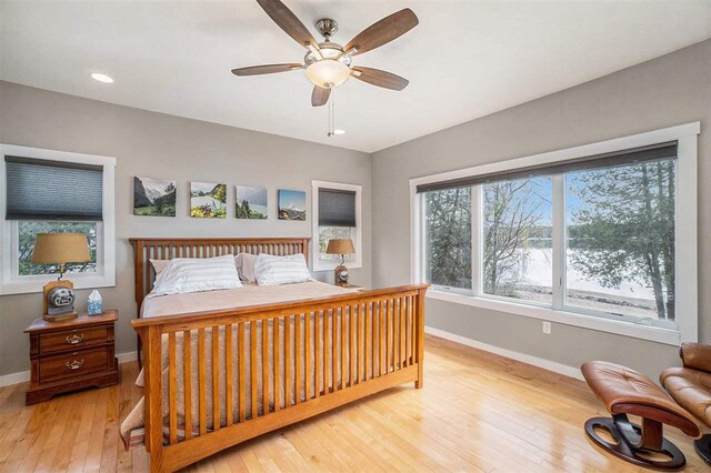bedroom with baseboards, a ceiling fan, a water view, and hardwood / wood-style flooring