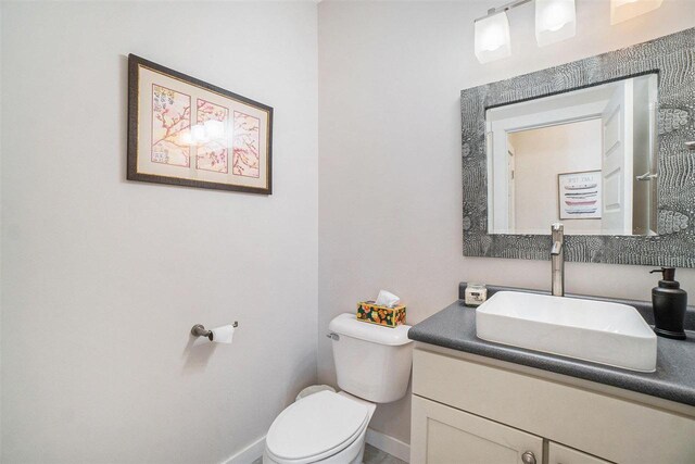 half bathroom featuring toilet, baseboards, and vanity