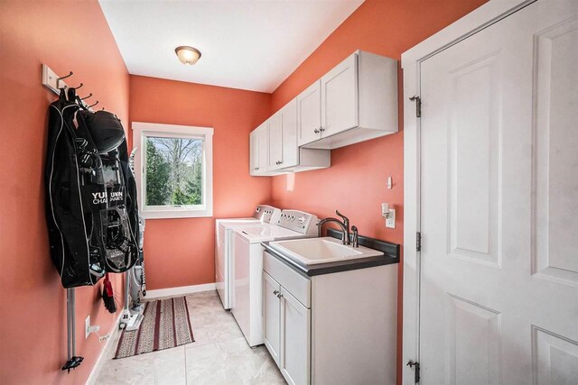 clothes washing area featuring separate washer and dryer, a sink, cabinet space, and baseboards