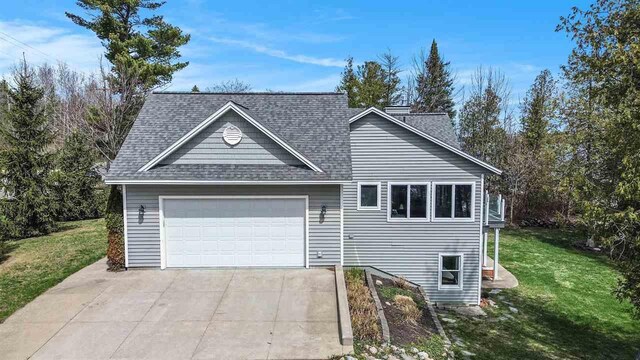 view of front facade with concrete driveway, an attached garage, a shingled roof, and a front lawn