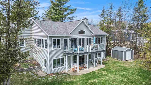 back of property with a lawn, an outbuilding, a storage unit, a patio, and a shingled roof