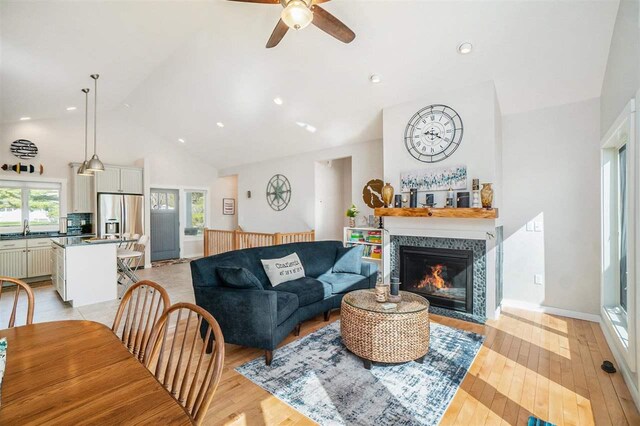 living room featuring light wood-type flooring, ceiling fan, high vaulted ceiling, and a tile fireplace