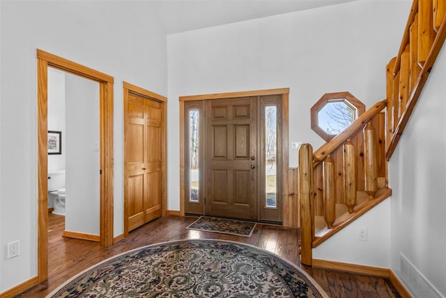 foyer entrance featuring a high ceiling, baseboards, visible vents, dark wood-style floors, and stairway