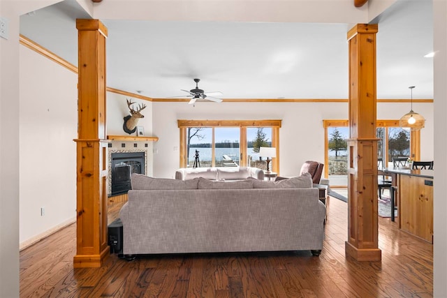 living room with crown molding, dark wood-style flooring, baseboards, ceiling fan, and a tiled fireplace