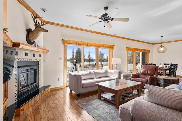 6650 S Beach Dr, Alanson, MI 49706 - living area featuring ceiling fan, a tiled fireplace, baseboards, ornamental molding, and hardwood / wood-style flooring