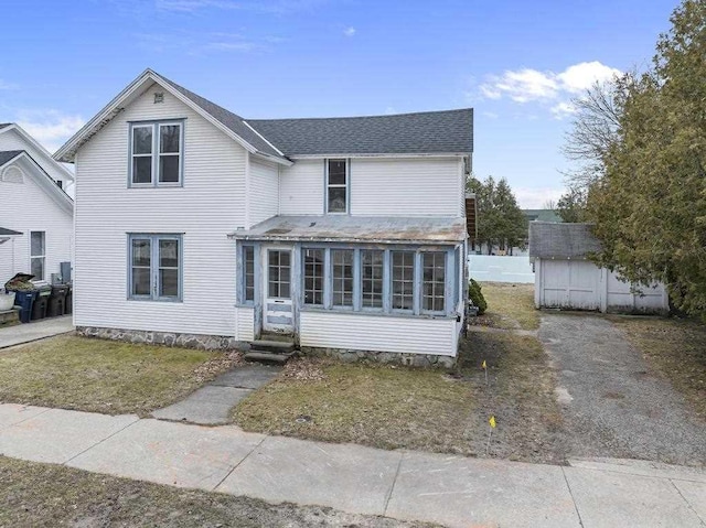 traditional-style home with a storage shed, a shingled roof, an outdoor structure, and a sunroom
