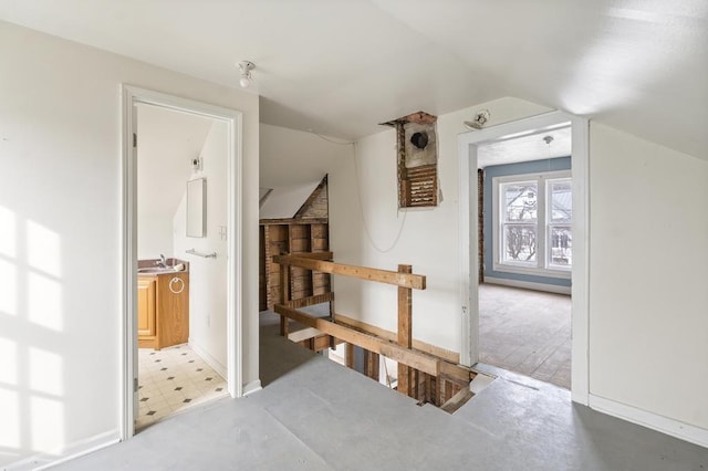 hall with a sink, tile patterned floors, vaulted ceiling, and an upstairs landing