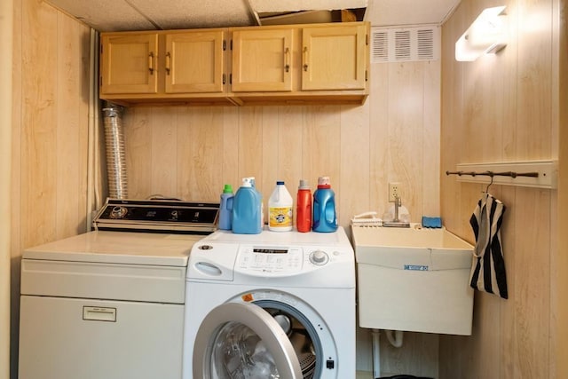 laundry room featuring a sink, wood walls, cabinet space, and washing machine and dryer