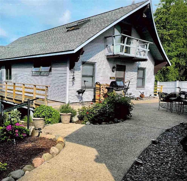 rear view of property featuring a patio, a shingled roof, fence, and a balcony