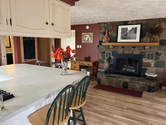 8118 E Mitchell St, Petoskey, MI 49770 - dining room featuring a stone fireplace, a textured ceiling, light wood-style flooring, and visible vents