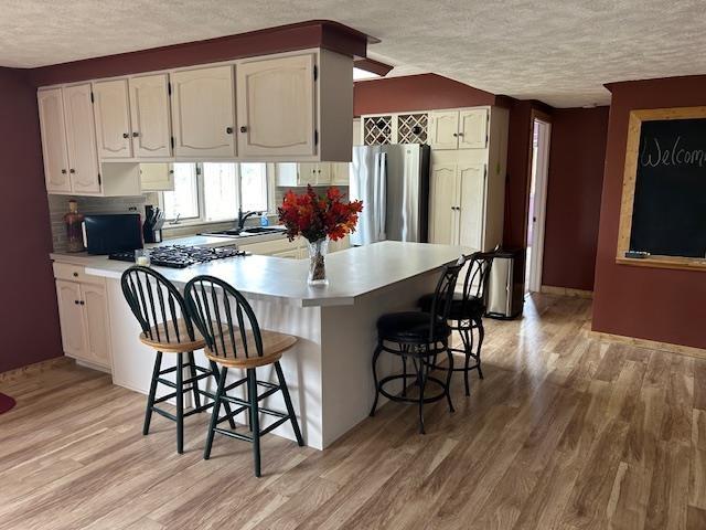 8118 E Mitchell St, Petoskey, MI 49770 - kitchen with a breakfast bar area, a textured ceiling, light wood-type flooring, white cabinets, and freestanding refrigerator