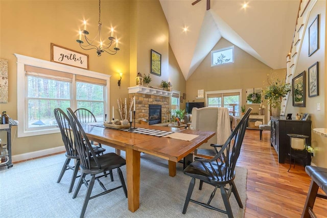 dining space with an inviting chandelier, light wood-type flooring, a fireplace, and high vaulted ceiling