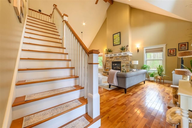 stairs with wood finished floors, baseboards, a stone fireplace, and high vaulted ceiling