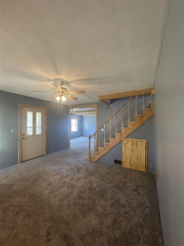4445 Howard Rd, Petoskey, MI 49770 - unfurnished living room with a textured ceiling, visible vents, ceiling fan, stairway, and carpet floors