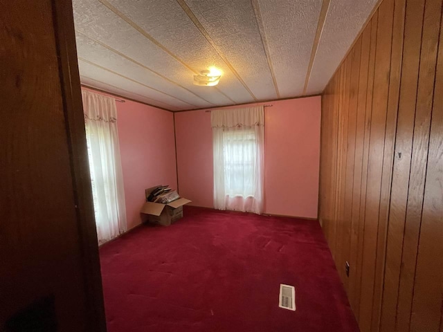 spare room featuring carpet, wood walls, visible vents, and a textured ceiling