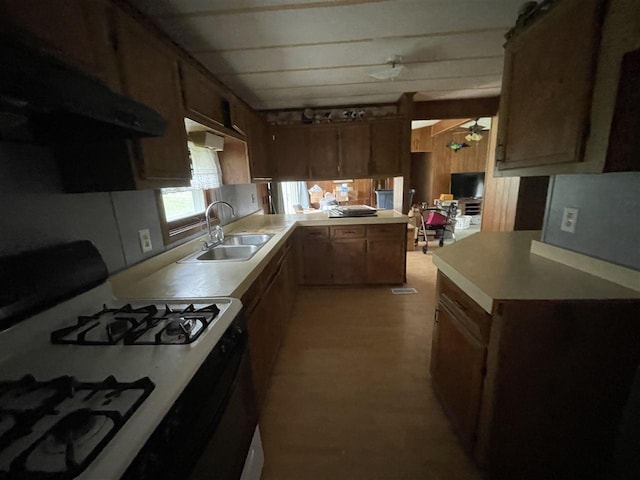 kitchen featuring a sink, a peninsula, ventilation hood, gas stove, and light countertops