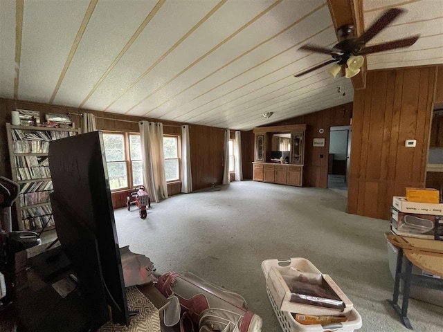 living area featuring lofted ceiling, wood walls, carpet, and ceiling fan