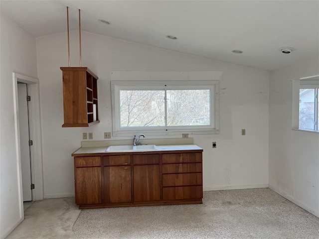 kitchen featuring a sink, vaulted ceiling, open shelves, light countertops, and brown cabinetry