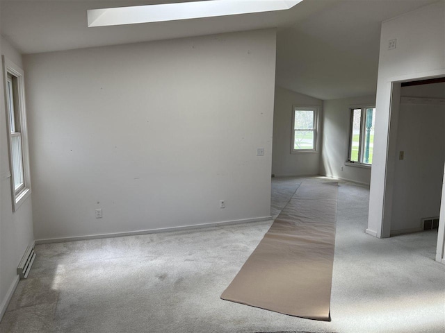 unfurnished room with carpet, a baseboard heating unit, vaulted ceiling, baseboards, and a skylight
