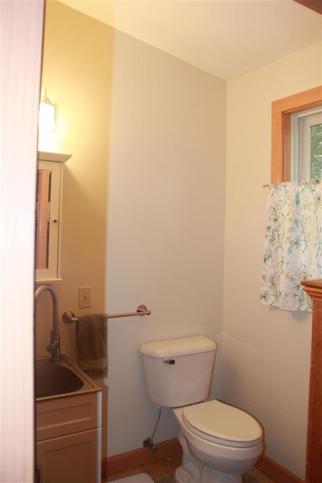 half bathroom with baseboards, toilet, and vanity