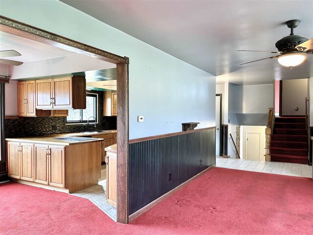 kitchen featuring a ceiling fan, light carpet, light tile patterned flooring, tasteful backsplash, and wainscoting