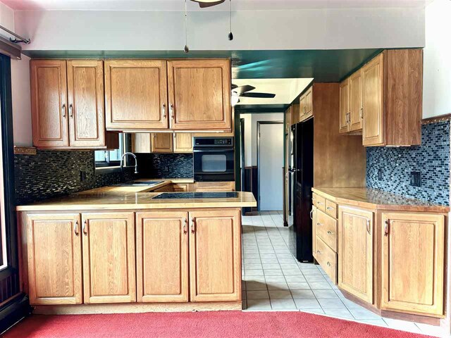 kitchen with a sink, ceiling fan, black appliances, a peninsula, and backsplash
