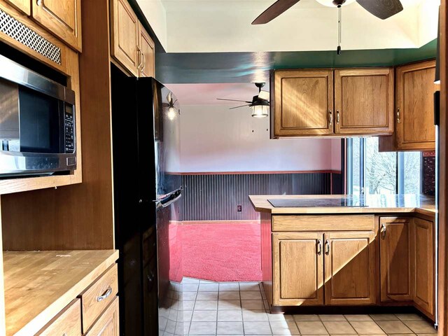 kitchen featuring a ceiling fan, freestanding refrigerator, stainless steel microwave, a wainscoted wall, and light tile patterned floors