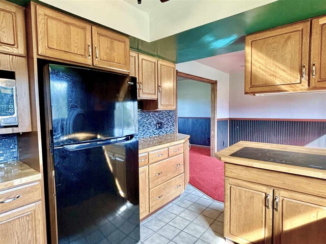 kitchen with black appliances, light countertops, light tile patterned floors, decorative backsplash, and wainscoting