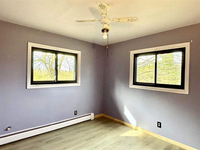 spare room featuring a baseboard heating unit, wood finished floors, baseboards, and ceiling fan
