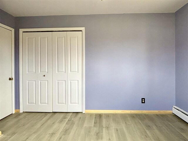 unfurnished bedroom featuring a baseboard radiator, wood finished floors, baseboards, and a closet