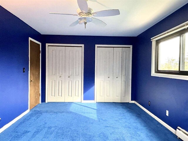 unfurnished bedroom featuring baseboard heating, baseboards, two closets, and carpet