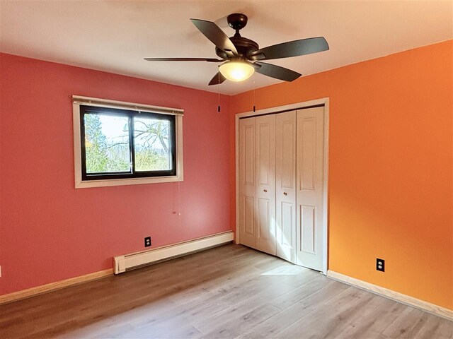 unfurnished bedroom with a baseboard heating unit, light wood-type flooring, baseboards, a closet, and ceiling fan