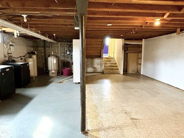 unfinished basement featuring a water pressure tank, stairway, washing machine and dryer, and tile patterned floors