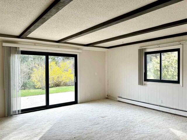 empty room featuring plenty of natural light, carpet floors, a textured ceiling, baseboard heating, and beamed ceiling