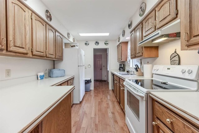 kitchen featuring white appliances, under cabinet range hood, light countertops, light wood-style flooring, and a sink
