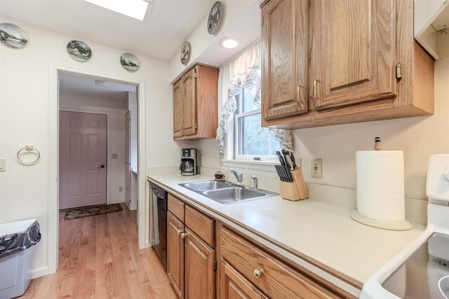 kitchen with a sink, black dishwasher, light countertops, light wood-type flooring, and brown cabinetry