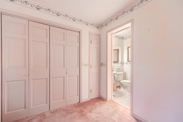 unfurnished bedroom featuring a closet, light colored carpet, and ensuite bath