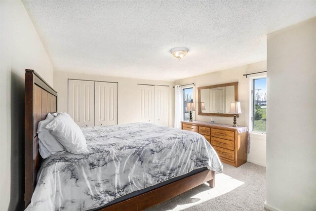 bedroom with light carpet, a textured ceiling, baseboards, and two closets
