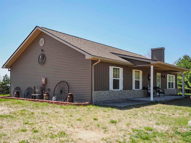 10300 Vista Ridge Dr, Alden, MI 49612 - view of home's exterior with a chimney, board and batten siding, stone siding, a shingled roof, and a patio area