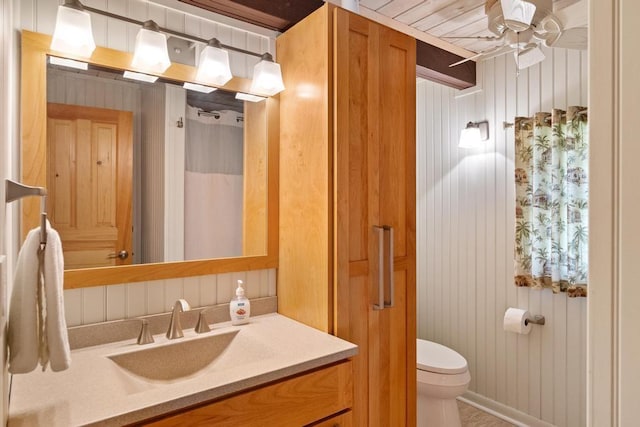 bathroom with toilet, ceiling fan, vanity, wooden walls, and a shower with shower curtain
