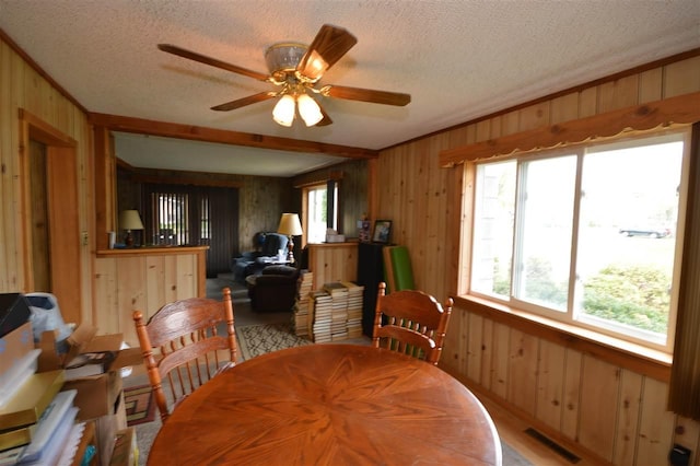 dining space featuring wooden walls, a textured ceiling, and a ceiling fan