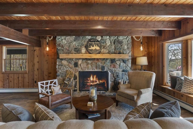 living room with wood-type flooring, wood walls, a baseboard heating unit, a stone fireplace, and beamed ceiling