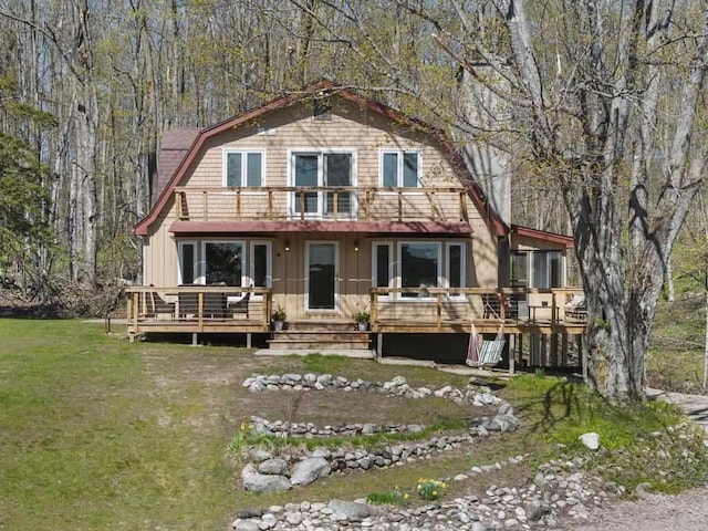 view of front of property with a gambrel roof, a balcony, a front yard, and a deck