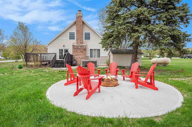 3190 Spring Dr, Boyne Falls, MI 49713 - back of property featuring a fire pit, a deck, a chimney, a lawn, and a storage shed