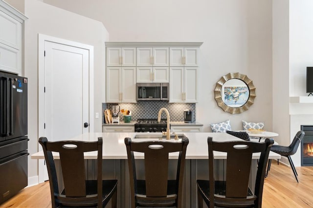 kitchen featuring stainless steel microwave, freestanding refrigerator, a sink, backsplash, and a center island with sink