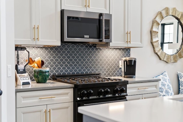 kitchen with stainless steel microwave, black range with gas stovetop, decorative backsplash, white cabinets, and light countertops