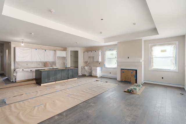 kitchen with a tray ceiling, white cabinetry, a center island, light wood-style floors, and baseboards