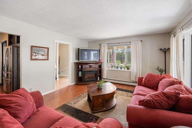 6141 S Old 31, Charlevoix, MI 49720 - living room with a baseboard heating unit, wood finished floors, a textured ceiling, a fireplace, and baseboards